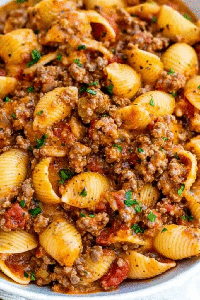 Creamy beef and shells pasta in a large skillet with ground beef, shell pasta, melted cheese, and rich tomato sauce garnished with fresh herbs
